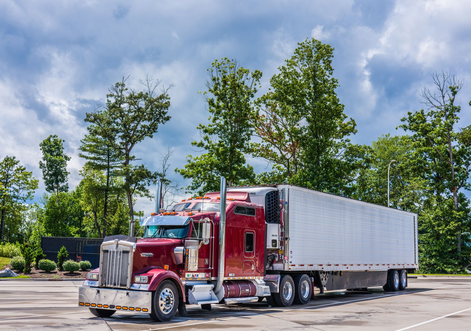 A striking red semi truck parked in a lush scenic area, showcasing modern transportation technology.