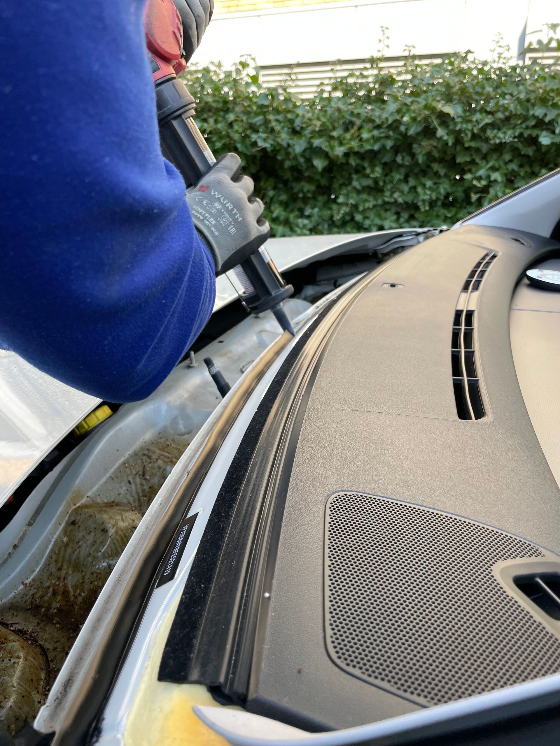 Detailed view of a mechanic repairing a car windshield using glue outdoors in Copenhagen.